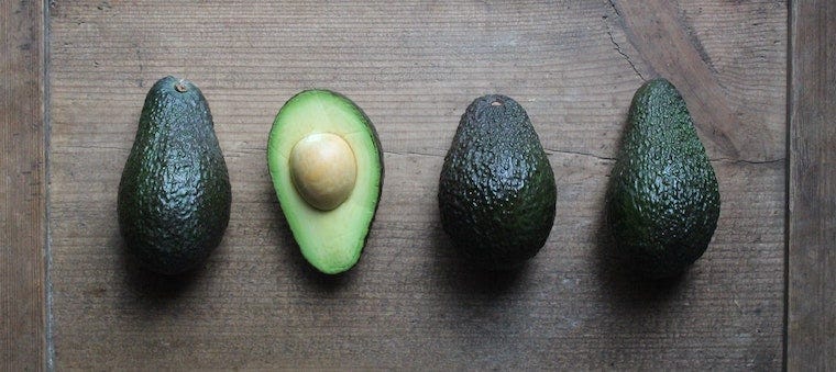 Three whole avocados and one half sliced avocado on a wooden cutting board - can cats eat avocado?
