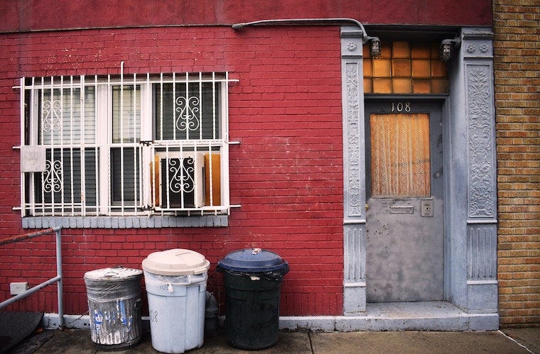 trash cans in front of a red brick well next to a door on a city block
