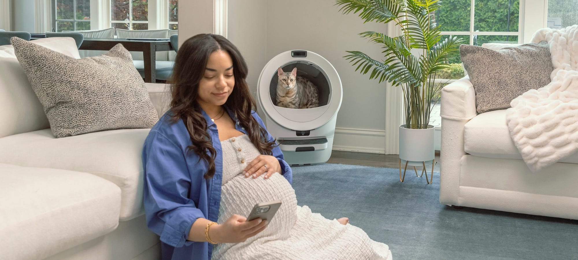 cat using self-cleaning litter box while pregnant woman looks at her phone