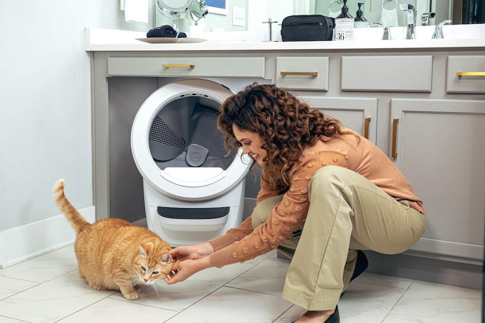 woman petting orange tabby cat in front of white Litter-Robot 4